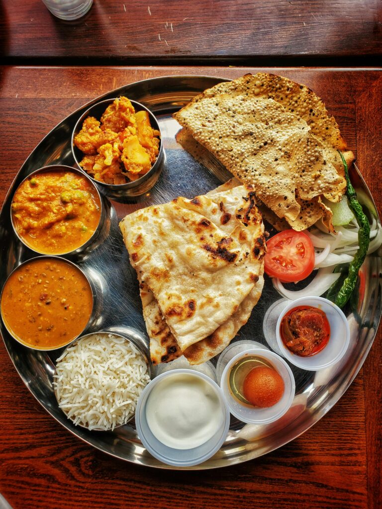 pexels-photo-8148149-8148149 Delicious Indian thali featuring naan, curries, and assorted dips on a tray.
